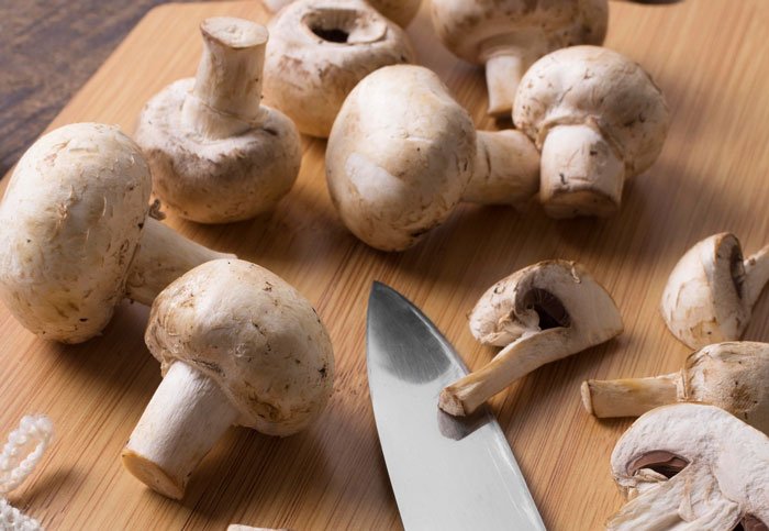 Fresh mushrooms and a kitchen knife on a wooden cutting board, highlighting fiber&rsquo;s role in removing cancer-causing chemicals.