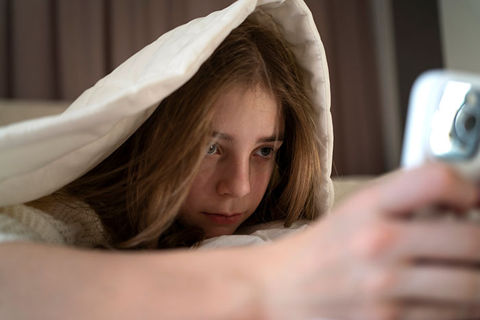 14-year-old girl looks tired and paranoid under blanket, showing signs of sleep deprivation from daily infant babysitting.
