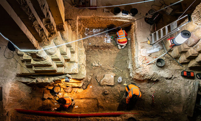 Archaeologists uncover a 400-year-old burial vault beneath church during restoration work with excavation tools and lighting.