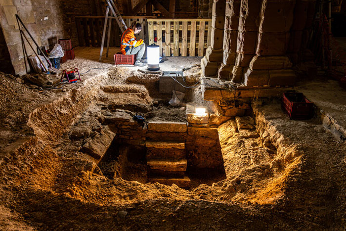 Archaeologist in safety vest examining a 400-year-old burial vault accidentally uncovered during church restoration.