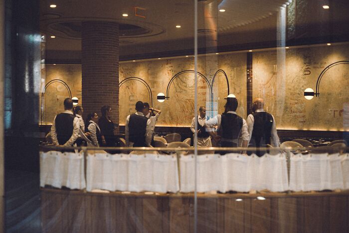 Group of waiters dressed in uniforms preparing for service inside a restaurant reflecting cultural norms that may shock Americans.