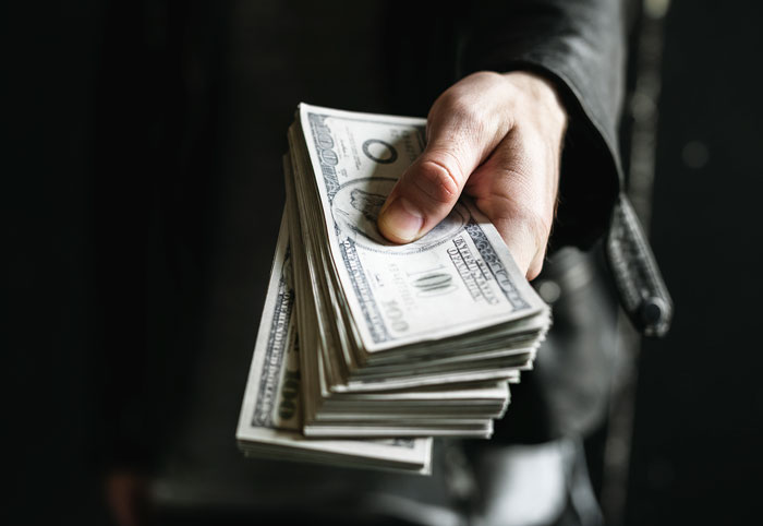 Hand holding a stack of hundred dollar bills symbolizing inheritance and financial dispute between best friends. Hand holding a stack of hundred dollar bills symbolizing inheritance and financial dispute between best friends.