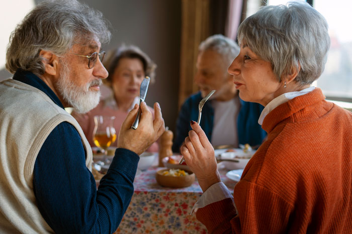 Older adults enjoying a meal together at a cozy indoor gathering, sharing conversation and food in a warm setting.