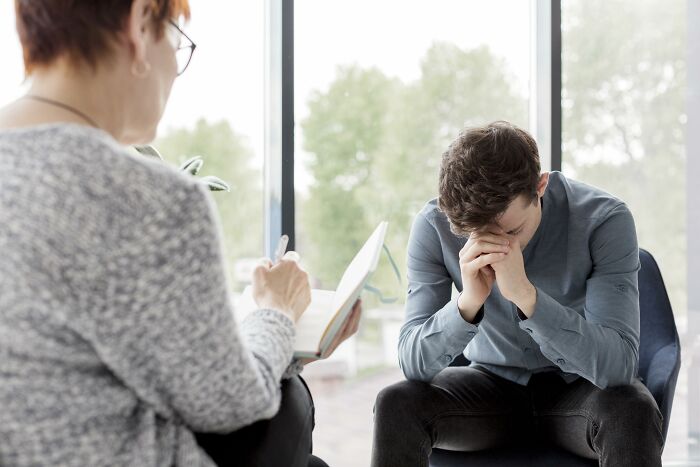 Therapist listening and taking notes while a stressed man sits with his head in hands during counseling session.