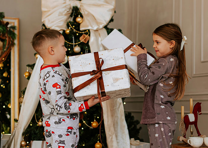 Two kids in festive pajamas exchanging Christmas gifts with decorations, reflecting funny and inappropriate things kids say.