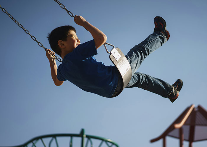 Boy swinging high on a playground swing, capturing playful and funny moments kids blurt out outdoors.
