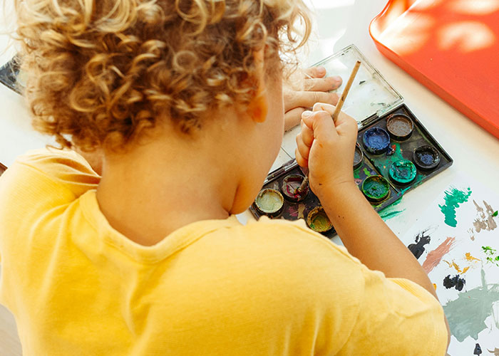 Child with curly hair painting with watercolors, capturing the funniest and most inappropriate things kids have blurted out.