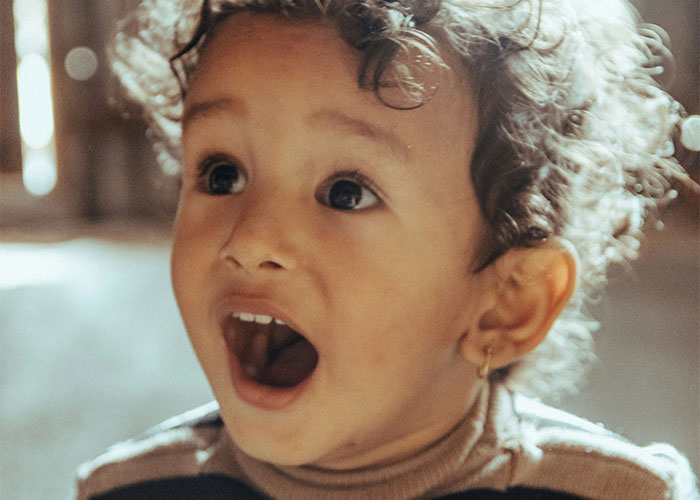 Young child with curly hair and open mouth expressing surprise, capturing funny and inappropriate kids' blurts by parents.