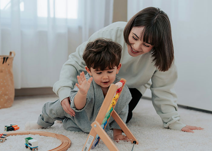 Mother and young child playing with wooden toys on carpet, capturing funny and inappropriate kids moments shared by parents