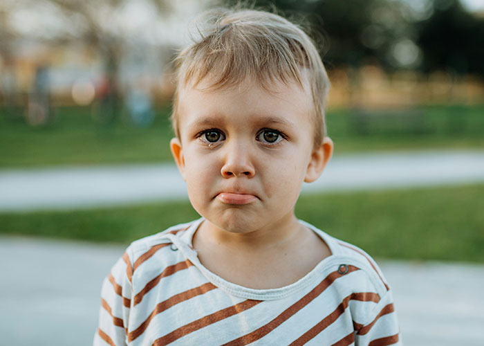 Toddler with sad expression outdoors, capturing the innocence behind funny and inappropriate kids' blurts shared by parents.