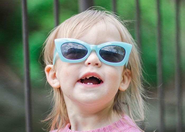Toddler wearing blue sunglasses outdoors, capturing the fun and unexpected moments kids blurt out.