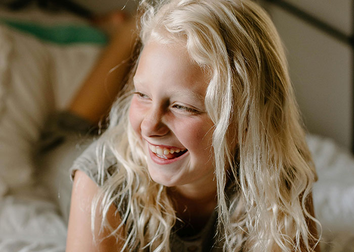 Smiling young girl with blonde hair laughing, capturing the funniest and most inappropriate things kids have blurted out.