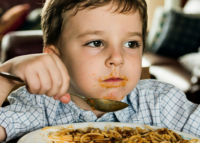 Young boy eating spaghetti with a messy face, illustrating funny and inappropriate things kids have blurted out.