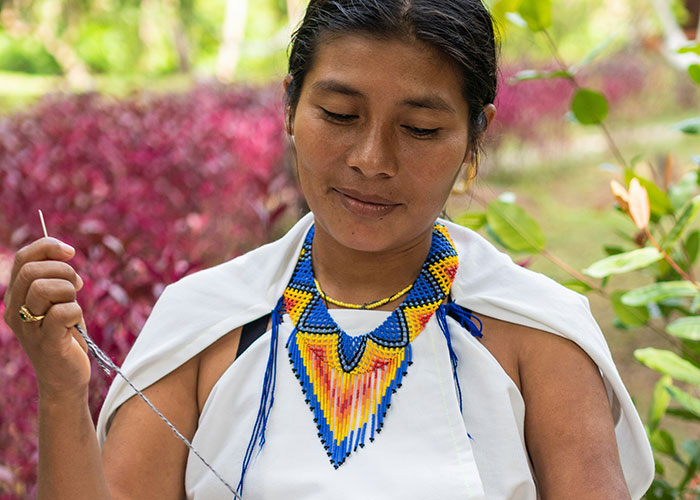Woman wearing colorful beaded necklace and traditional clothing, engaged in a crafting activity outdoors, related to funny kids blurts.