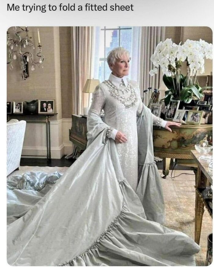 Elegant woman in a grand room wearing a long dress resembling a fitted sheet, humorously illustrating struggle with folding sheets.