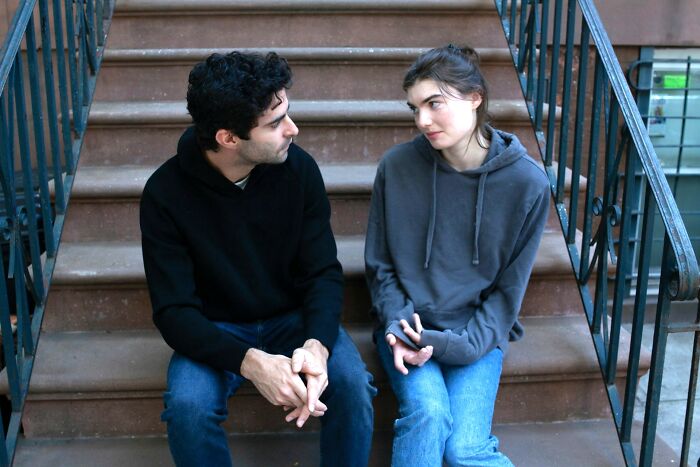 A man and woman sitting on outdoor stairs having a serious conversation about twins and pregnancy.