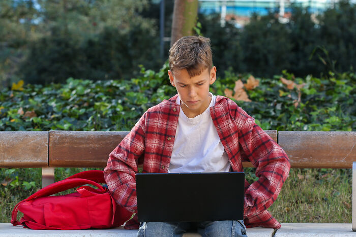 Boy in a red plaid shirt using a laptop outdoors, illustrating teachers sharing horror stories about younger generations' abilities.