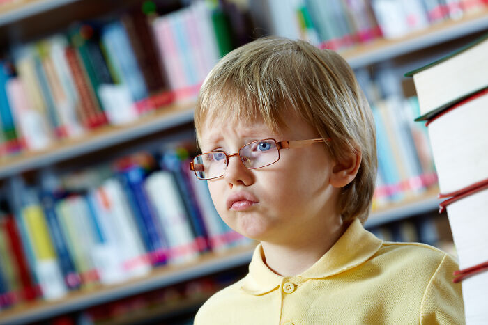 Young student in glasses looking confused in library, illustrating teachers' stories about nose-diving abilities of younger generations.