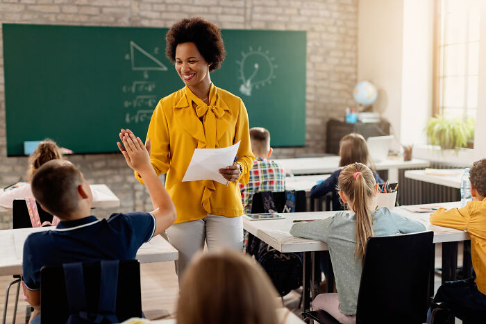 Teacher in a bright classroom interacting with students, highlighting challenges faced with younger generations' abilities.