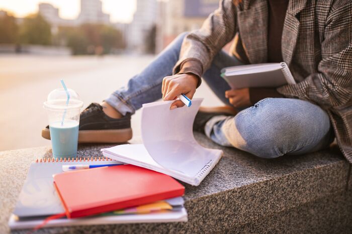 Student sitting outdoors with notebooks and pen, illustrating the nose-diving abilities of the younger generations in education.
