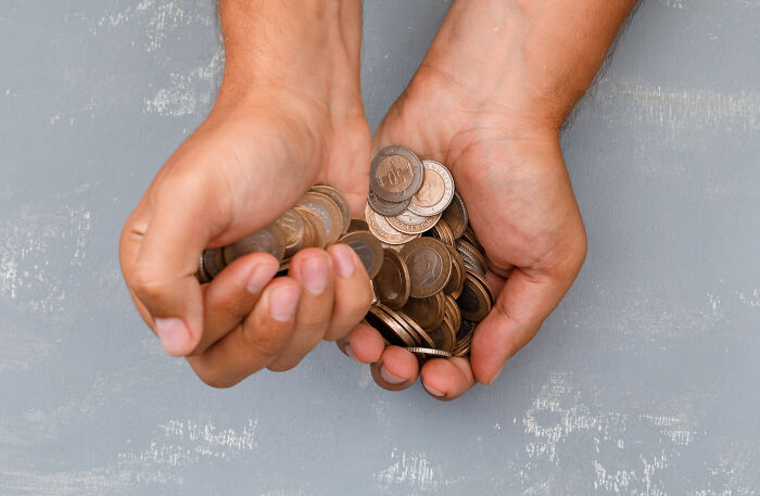 Hands holding a large amount of coins tightly, illustrating the nose-diving abilities of the younger generations concept.