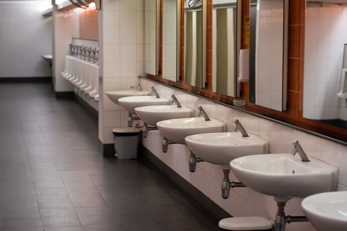 Public restroom sinks and mirrors in a school bathroom symbolizing teachers sharing horror stories about younger generations' declining abilities.