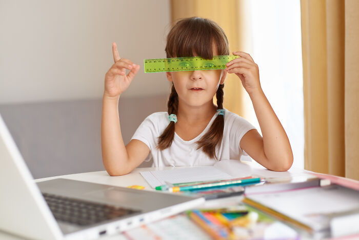 Young girl at desk holding a green ruler over her eyes, illustrating challenges in the nose-diving abilities of younger generations.