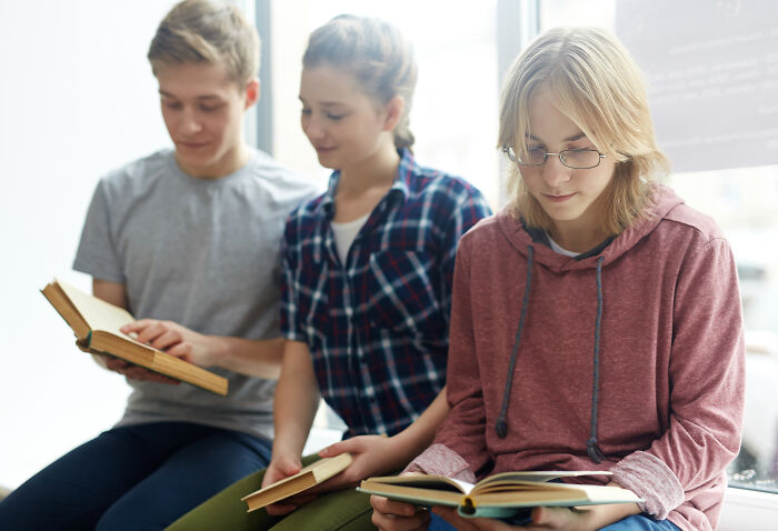 Three teenagers sitting and reading books, illustrating teachers sharing horror stories about younger generations’ abilities.