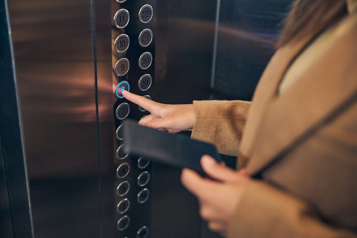 Person pressing elevator button inside a metallic elevator, illustrating challenges of being big in Japan for foreigners.