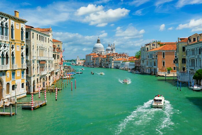 Venice canal with boats and historic buildings under a blue sky, illustrating popular travel destinations to avoid.