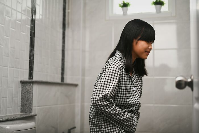 Young woman in checkered shirt leaning forward in bathroom, reflecting on dark, spicy, and heartfelt secrets in a relationship.