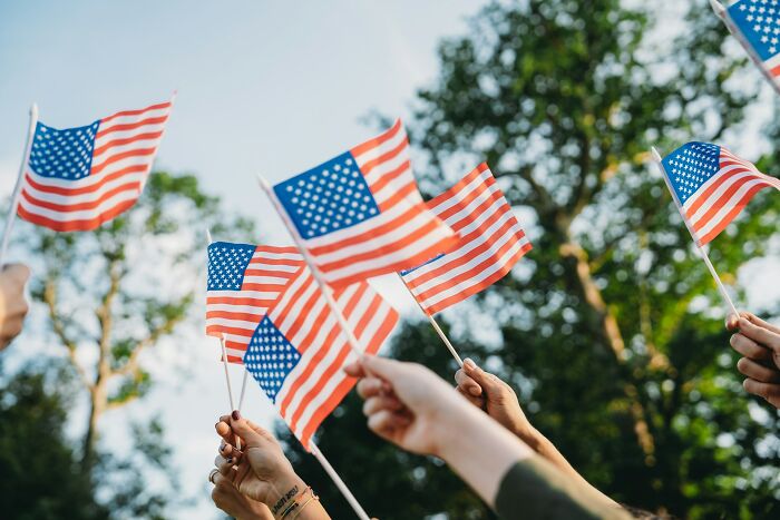 Multiple hands holding and waving American flags outdoors, reflecting opinions on current situation and social awareness.