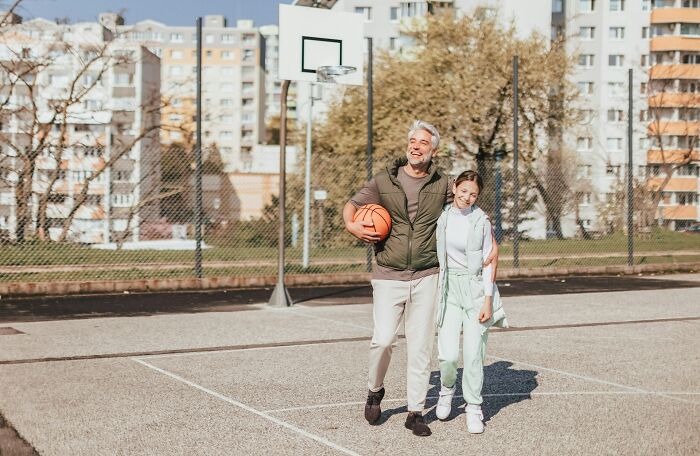 Older man holding basketball with younger woman on outdoor court, illustrating moments people realized close friend was a jerk.