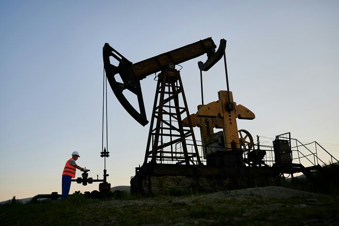 Worker in safety gear operating large oil pumpjack at sunset illustrating dinosaur facts about natural resources.