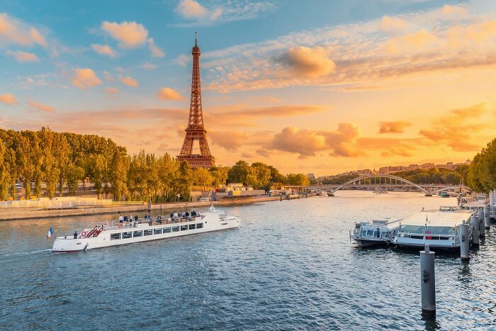 Seine River cruise boat passing near Eiffel Tower during sunset, illustrating travel destinations tourists may avoid.