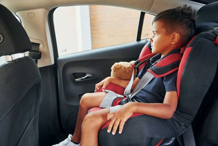 Young boy sitting in a car seat holding a teddy bear, reflecting on experiences with the worst parents seen.