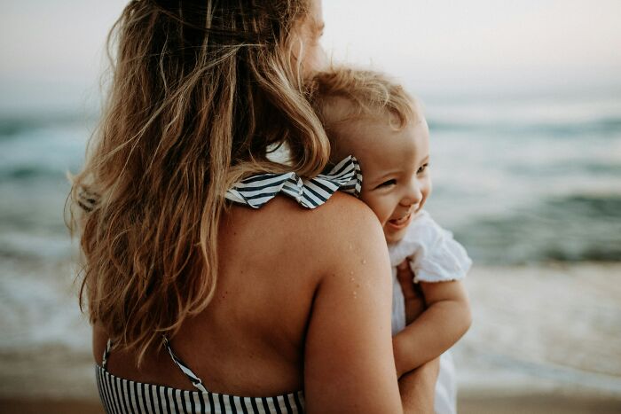 Mother holding smiling baby near the ocean, illustrating the emotional experience of postpartum OCD in new mothers.