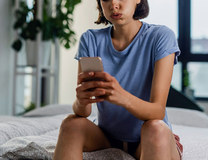 Young woman in blue shirt looking concerned while using smartphone, highlighting romance scam warning and silent treatment. Young woman in blue shirt looking concerned while using smartphone, highlighting romance scam warning and silent treatment.
