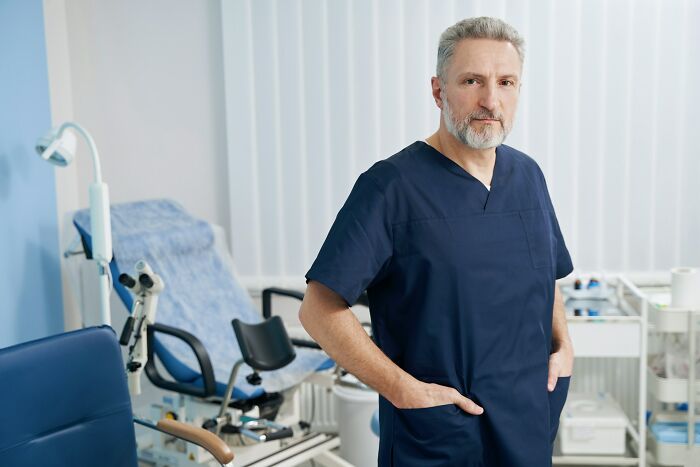Middle-aged doctor in navy scrubs standing confidently in a modern medical office, reflecting no peaceful solution scenario.