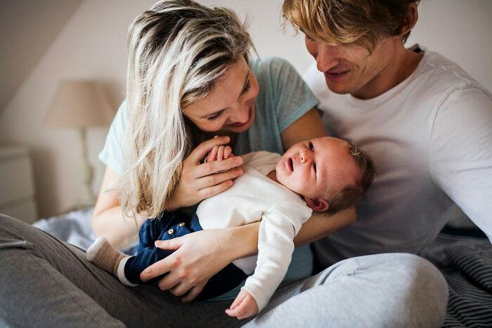 Young parents holding and smiling at their newborn baby, sharing a tender moment in a cozy home setting.
