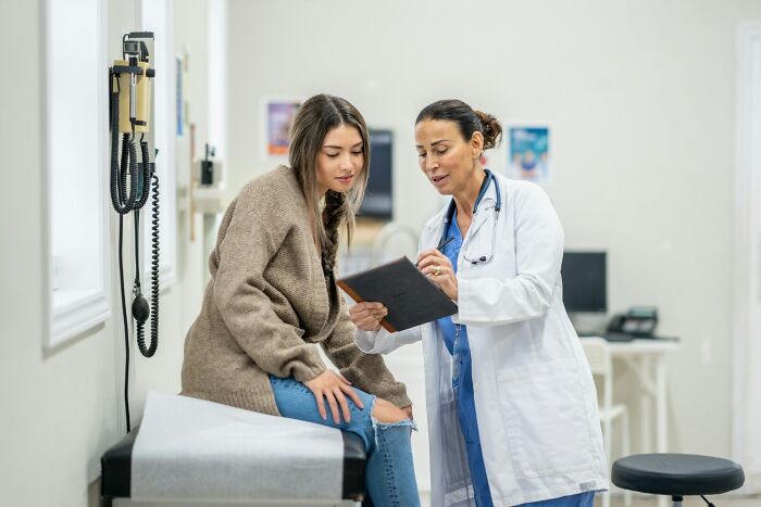 Female doctor explaining medical results to a young woman in a clinic, highlighting frustrating experiences with dismissive doctors.