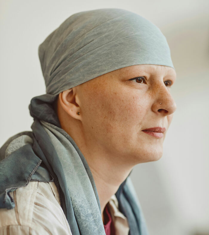 Person wearing a gray headscarf, looking thoughtfully to the side, conveying strength and resilience in a medical setting.
