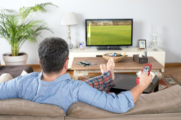 Man relaxing on couch watching TV with remote in hand, illustrating industries impacted by millennials' changing habits.