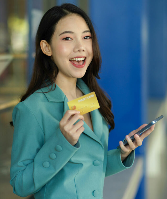 Young woman happily holding a credit card and smartphone, symbolizing moments people drove away potential life partners.