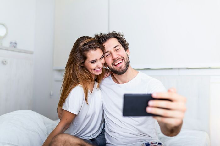 A couple smiling and taking a selfie together, illustrating behaviors that may indicate someone is insecure.
