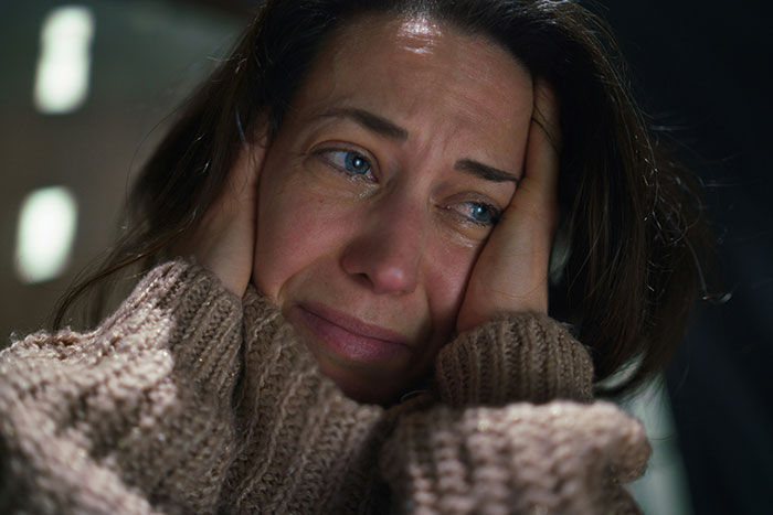 Woman with a distressed expression wearing a knitted sweater, representing psoriasis struggle before a wedding event conflict.