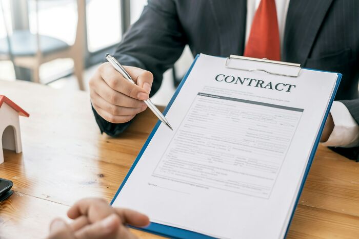 Person in suit pointing at contract with pen during a discussion about sneaky terms and conditions before signing.