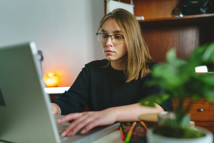 Young woman wearing glasses working on laptop, reflecting on dark and heartfelt secrets people keep from their lovers.