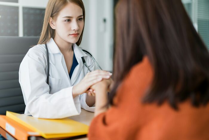 Female oncologist in white coat holding patient's hand during consultation, emphasizing tobacco avoidance advice.