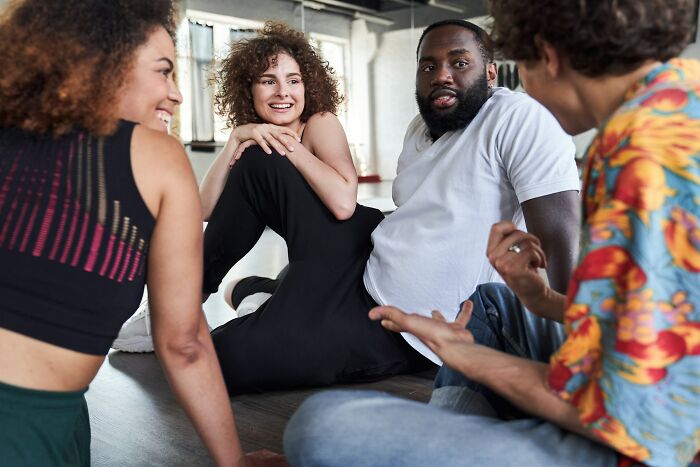A diverse group of people sitting on the floor, engaged in conversation displaying behaviors that may indicate insecurity.